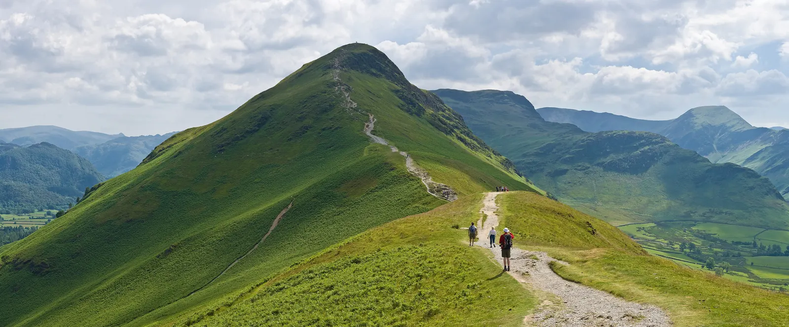 Walkers on the path along the grassy north ridge of Catbells, with the pointed summit ahead