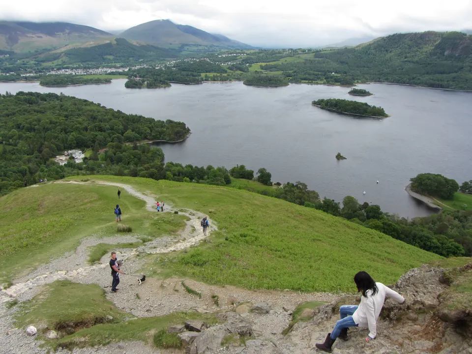 Walkers using their hands on a rocky step on the ridge of Catbells, with Derwentwater below