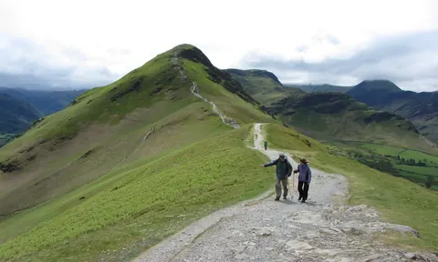 Two walkers on the stony ridge path on Skelgill Bank with the summit cone of Catbells ahead
