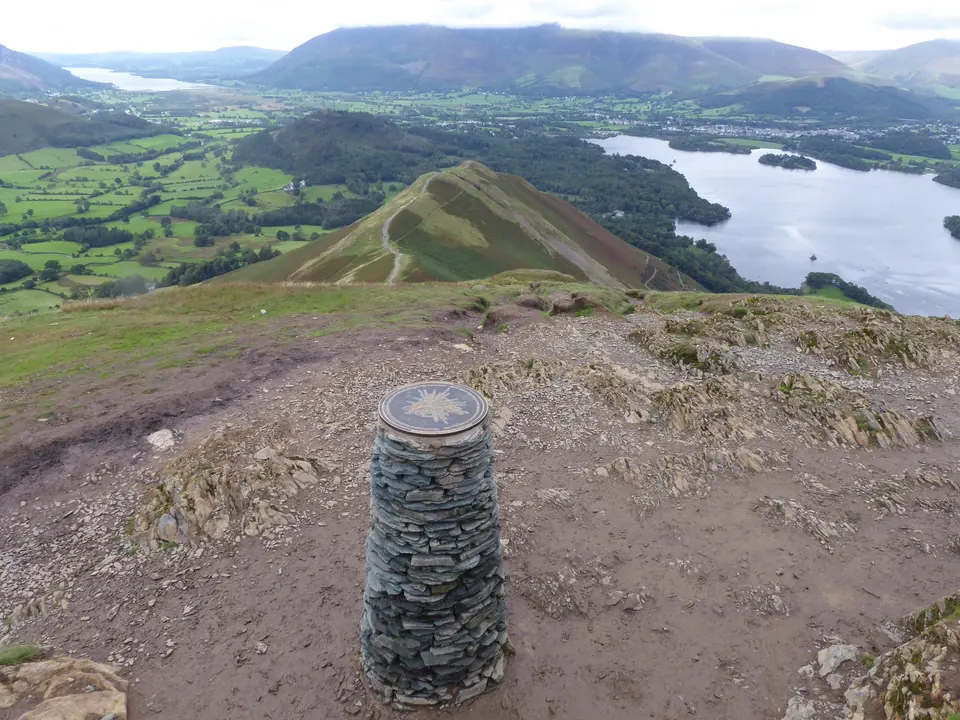 The stone view indicator on the bare rock summit of Catbells, with Skelgill Bank and Derwentwater below