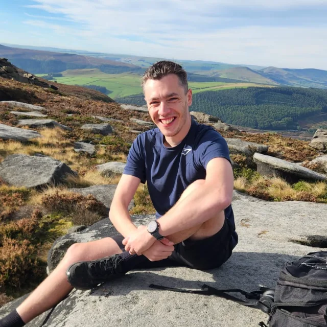 Chris Davidson sitting on a gritstone edge, with a valley behind